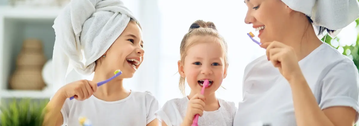 Mamma e figlie sorridenti si lavano i denti insieme, promuovendo l’igiene orale in famiglia